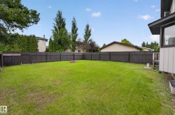 Expansive backyard with a manicured lawn, full perimeter privacy fence, and mature trees - 
