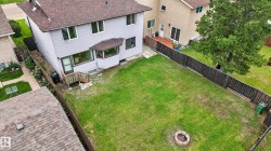 Expansive rear yard featuring a manicured lawn, established privacy fencing, a ground-level fire pit, a lower patio, and a sunroom extension - 