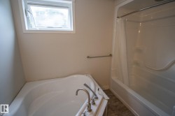 Bathroom featuring a built-in jetted tub, a separate shower/tub combination with a shower curtain, and a window with white trim - 