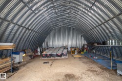 Expansive arched metal structure featuring corrugated metal walls and ceiling, exposed metal framing, and a gravel floor - 