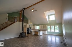 Spacious open-concept living area featuring a wood-burning stove, vaulted ceilings, and an exposed wooden beam - 