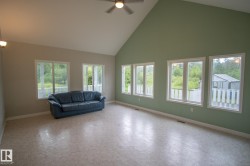 Spacious room featuring a vaulted ceiling with a ceiling fan, multiple windows with white trim, and light-toned flooring - 