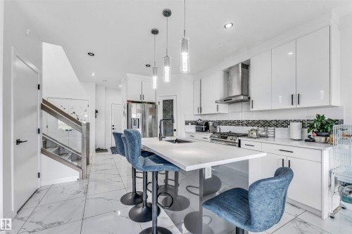 Modern kitchen featuring white cabinetry, a large center island with seating, stainless steel appliances, and sleek pendant lighting - 5809 65 Street, Beaumont, AB - Indoor Photo Showing Kitchen With Upgraded Kitchen