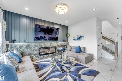 Living area featuring a textured accent wall, an integrated electric fireplace with a stone surround, and an open staircase with glass panel railings - 5809 65 Street, Beaumont, AB - Indoor Photo Showing Living Room With Fireplace
