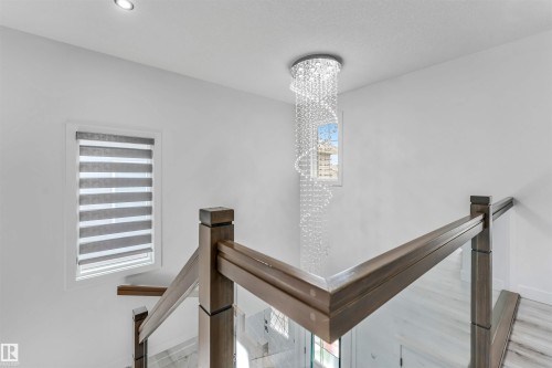 Elegant crystal chandelier illuminating a contemporary stairwell featuring wood newel posts, glass railings, and light wood-finish flooring - 5809 65 Street, Beaumont, AB - Indoor Photo Showing Other Room