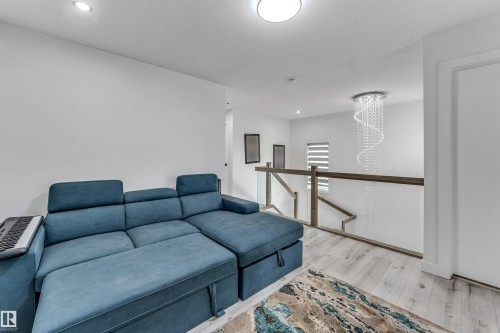 Upper level featuring light wood-finish flooring, a contemporary chandelier, and a glass-paneled railing with a wood top - 5809 65 Street, Beaumont, AB - Indoor
