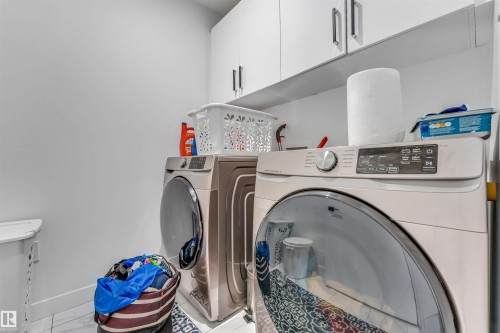 Dedicated laundry area featuring white upper cabinetry with brushed nickel pulls, a white baseboard, and light-toned tile flooring - 5809 65 Street, Beaumont, AB - Indoor Photo Showing Laundry Room