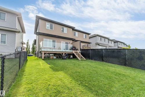 Rear exterior featuring a spacious lawn, large elevated deck with glass railing, and a walk-out lower level - 5809 65 Street, Beaumont, AB - Outdoor With Deck Patio Veranda