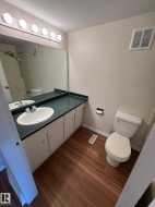 Bathroom featuring wood-finish flooring, a vanity with an integrated sink, a dark countertop, and a wall-mounted mirror - 