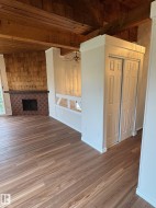 Open-concept living area featuring wood-finish flooring, exposed beam ceiling, a brick-surround fireplace with a wood mantel, and an integrated built-in bench seating area - 