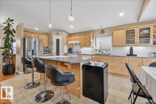 Spacious kitchen featuring light wood cabinetry, stainless steel appliances, an island with countertop seating, a subway tile backsplash, and ceramic tile flooring - 6050 164A Avenue, Edmonton, AB - Indoor Photo Showing Kitchen With Double Sink With Upgraded Kitchen