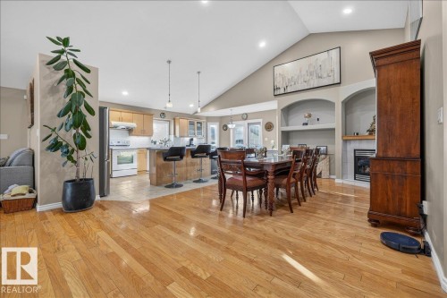 Open-concept living area featuring vaulted ceilings, wood-finish flooring, a kitchen island with seating, a built-in fireplace, and recessed lighting - 6050 164A Avenue, Edmonton, AB - Indoor Photo Showing Other Room