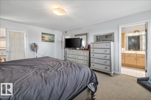 Carpeted room featuring a ceiling-mounted light fixture, white walls, and a door leading to a bathroom - 6050 164A Avenue, Edmonton, AB - Indoor Photo Showing Bedroom