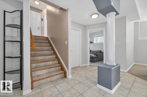Tiled entryway featuring a staircase with wood-finish handrails and carpeted treads, alongside a structural pillar with a decorative base - 6050 164A Avenue, Edmonton, AB - Indoor Photo Showing Other Room