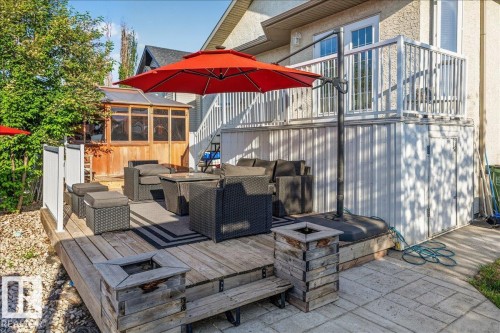 Multi-level outdoor living space featuring a wooden deck with a built-in fire pit, a patio area with stamped concrete, and a covered sunroom structure - 6050 164A Avenue, Edmonton, AB - Outdoor With Deck Patio Veranda With Exterior