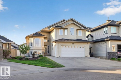 Stucco exterior with a prominent arched window, multi-paned garage door, and a paved driveway - 6050 164A Avenue, Edmonton, AB - Outdoor With Facade