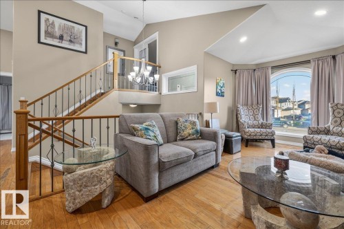 Vaulted ceiling living space featuring wood-finish flooring, a grand staircase with wrought iron spindles, and a large arched window - 6050 164A Avenue, Edmonton, AB - Indoor Photo Showing Living Room