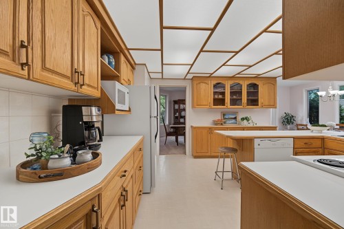 Kitchen featuring extensive wood cabinetry, white countertops, a built-in dishwasher, and a full-size refrigerator - 9516 146 Street, Edmonton, AB 