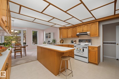 Kitchen featuring wood cabinetry, a center island with countertop, and an electric range with overhead ventilation - 9516 146 Street, Edmonton, AB 