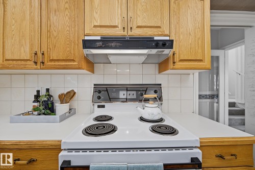 Kitchen featuring light wood cabinetry, white tile backsplash, a white electric range, and light-colored countertops - 9516 146 Street, Edmonton, AB 