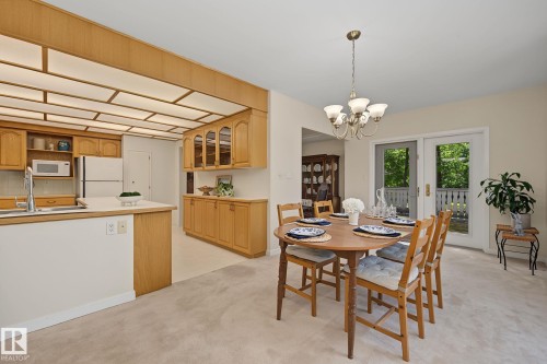 Dining area featuring a brass chandelier, neutral carpeting, and white sliding doors opening to a balcony - 9516 146 Street, Edmonton, AB 