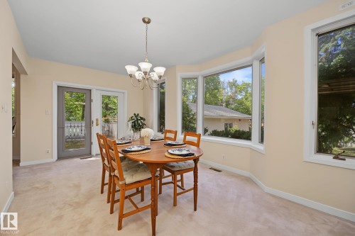 Dining space featuring a multi-paned bay window, neutral carpeting, and a polished brass chandelier - 9516 146 Street, Edmonton, AB 
