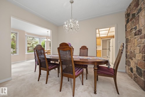 Dining area featuring a stone accent wall, neutral carpet, and a crystal chandelier - 9516 146 Street, Edmonton, AB 