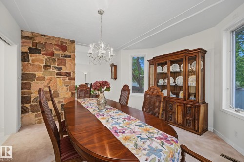 Dining area featuring a stone accent wall, bay window, chandelier lighting, and light-toned carpeting - 9516 146 Street, Edmonton, AB 