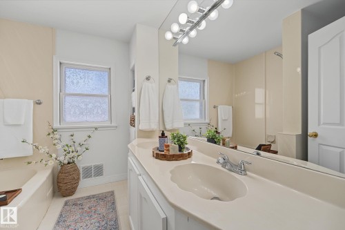 Bathroom featuring an integrated countertop and sink, a vanity mirror with a light fixture, and a window with privacy glass - 9516 146 Street, Edmonton, AB 