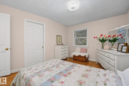 Bedroom featuring light-colored walls, wood-finish flooring, a white trim window, and a ceiling-mounted light fixture - 9516 146 Street, Edmonton, AB 