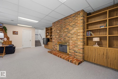 Brick fireplace with hearth, built-in shelving, wood-finish cabinetry, drop ceiling, and light-colored carpeting - 9516 146 Street, Edmonton, AB 