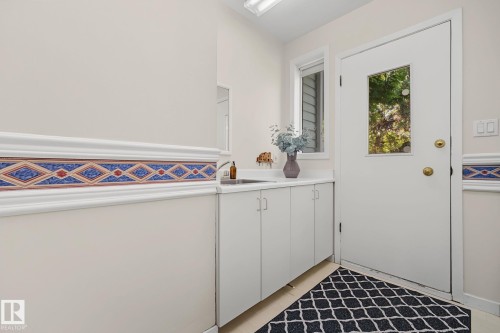 Utility room featuring a built-in countertop, undermount sink with a gooseneck faucet, white cabinetry, and a windowed exterior door - 9516 146 Street, Edmonton, AB 