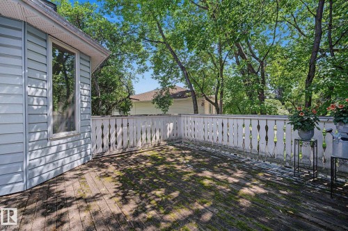 Expansive wood deck with decorative baluster railing, providing an outdoor extension to the home's light blue siding and large window - 9516 146 Street, Edmonton, AB 