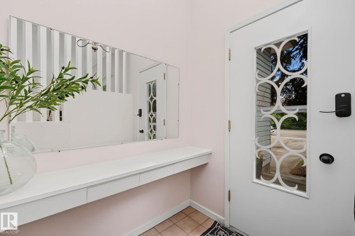 Entryway featuring a white door with decorative glass inlay, an integrated smart lock system, a floating console with drawer storage, a large wall-mounted mirror, and tile flooring - 9516 146 Street, Edmonton, AB 