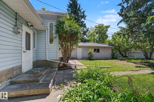 Spacious backyard featuring a detached garage, mature trees, and a concrete pathway leading to the home's rear entrance - 9516 146 Street, Edmonton, AB 