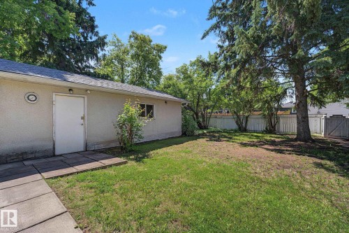 Spacious backyard featuring a stucco outbuilding, mature trees, a white privacy fence, and a concrete paver walkway - 9516 146 Street, Edmonton, AB 