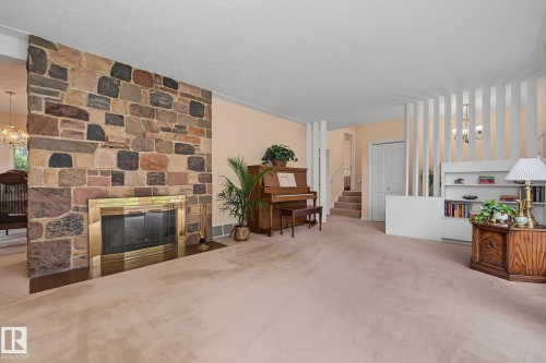 Spacious room featuring a stone fireplace with a brass-trimmed firebox, plush carpeting, and built-in shelving - 9516 146 Street, Edmonton, AB 