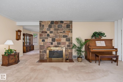 Living area featuring a stone accent wall with a built-in fireplace, light-colored carpeting, and a cased opening leading to an additional space - 9516 146 Street, Edmonton, AB 
