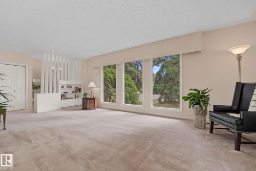 Spacious living area featuring expansive windows, neutral carpeting, and a built-in shelving unit - 9516 146 Street, Edmonton, AB 