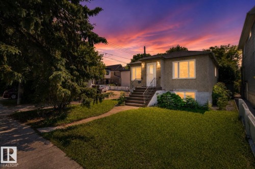 Stucco exterior featuring multiple windows and a prominent front entrance with stone steps and metal railings - 10607 73 Ave, Edmonton, AB 