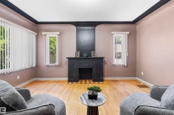 Living area featuring a black fireplace with a mantel, light wood-finish flooring, two large windows with vertical blinds, and dark ceiling trim - 