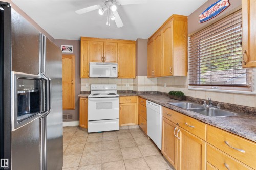 Kitchen featuring light wood cabinetry, a dual basin stainless steel sink, tiled backsplash, and light-toned tile flooring - 10607 73 Ave, Edmonton, AB 