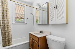 Bathroom featuring a built-in tub with a shower, single vanity with wood-finish cabinetry and a light-colored countertop, wall-mounted mirrored medicine cabinet, and a louvered wall cabinet - 