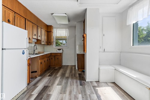 Kitchen area featuring wood-finish flooring, wood cabinetry, built-in banquette seating, and white appliances - 11619 123 Street, Edmonton, AB 