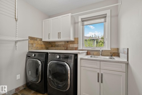 Dedicated utility space featuring a built-in basin sink, white cabinetry, slate backsplash, and light-toned countertops - 9 Greenfield Wynd, Fort Saskatchewan, AB - Indoor Photo Showing Laundry Room
