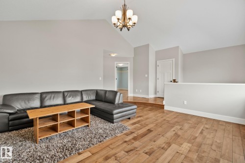 Vaulted ceilings enhance this living area featuring wood-finish flooring, a decorative chandelier, and light gray wall tones - 9 Greenfield Wynd, Fort Saskatchewan, AB - Indoor Photo Showing Living Room