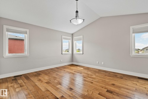 Vaulted ceiling room featuring hardwood flooring, multiple windows with white trim, a modern semi-flush mount light fixture, and light gray wall paint - 9 Greenfield Wynd, Fort Saskatchewan, AB - Indoor Photo Showing Other Room
