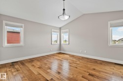Vaulted ceiling room featuring hardwood flooring, multiple windows with white trim, a modern semi-flush mount light fixture, and light gray wall paint - 