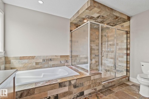 Bathroom featuring a walk-in glass shower, a built-in soaking tub, natural stone-finish tile flooring, and natural stone-finish tile surround - 9 Greenfield Wynd, Fort Saskatchewan, AB - Indoor Photo Showing Bathroom