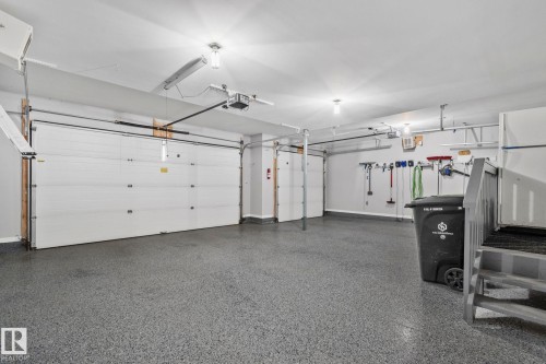 Spacious garage featuring two sectional doors, a durable epoxy-coated floor, overhead lighting, and built-in wall storage solutions - 9 Greenfield Wynd, Fort Saskatchewan, AB - Indoor Photo Showing Garage